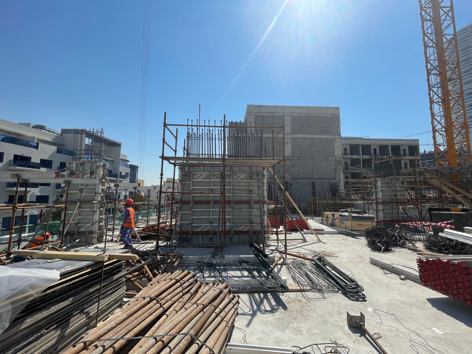 Pearl House By Imtiaz Construction site with scaffolding, building materials, and workers under a bright blue sky.